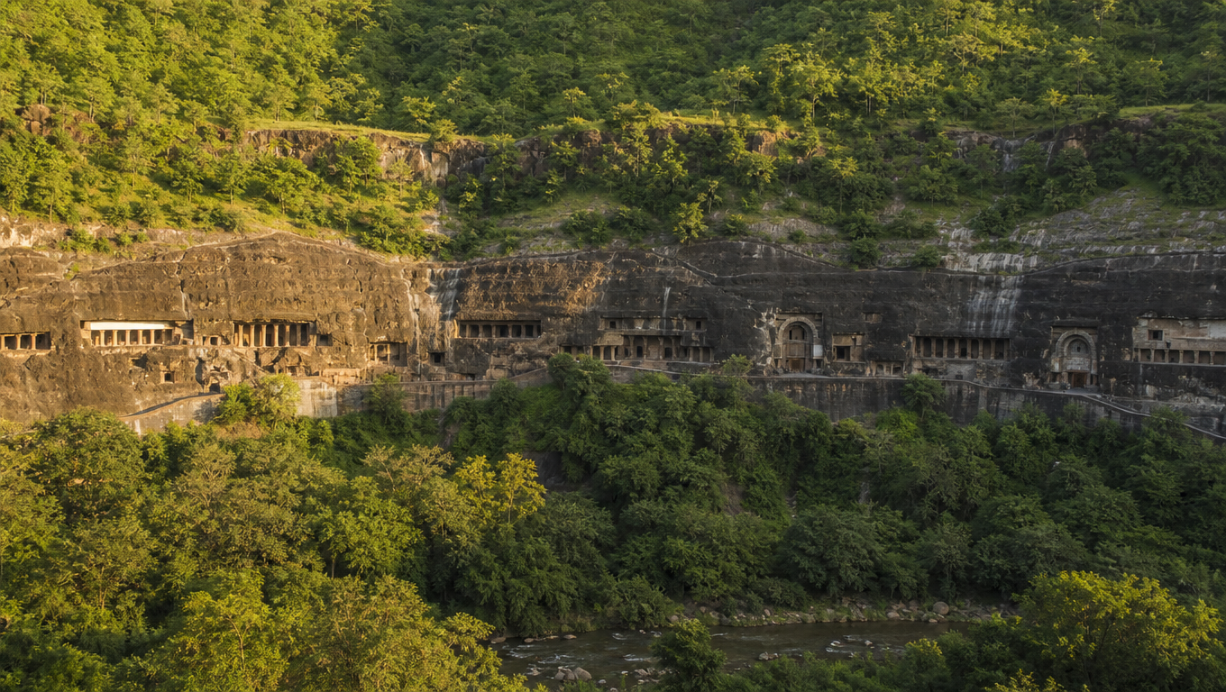 The row of carved Ajanta cave facades cut into the curved basalt cliff above the Waghora river gorge.