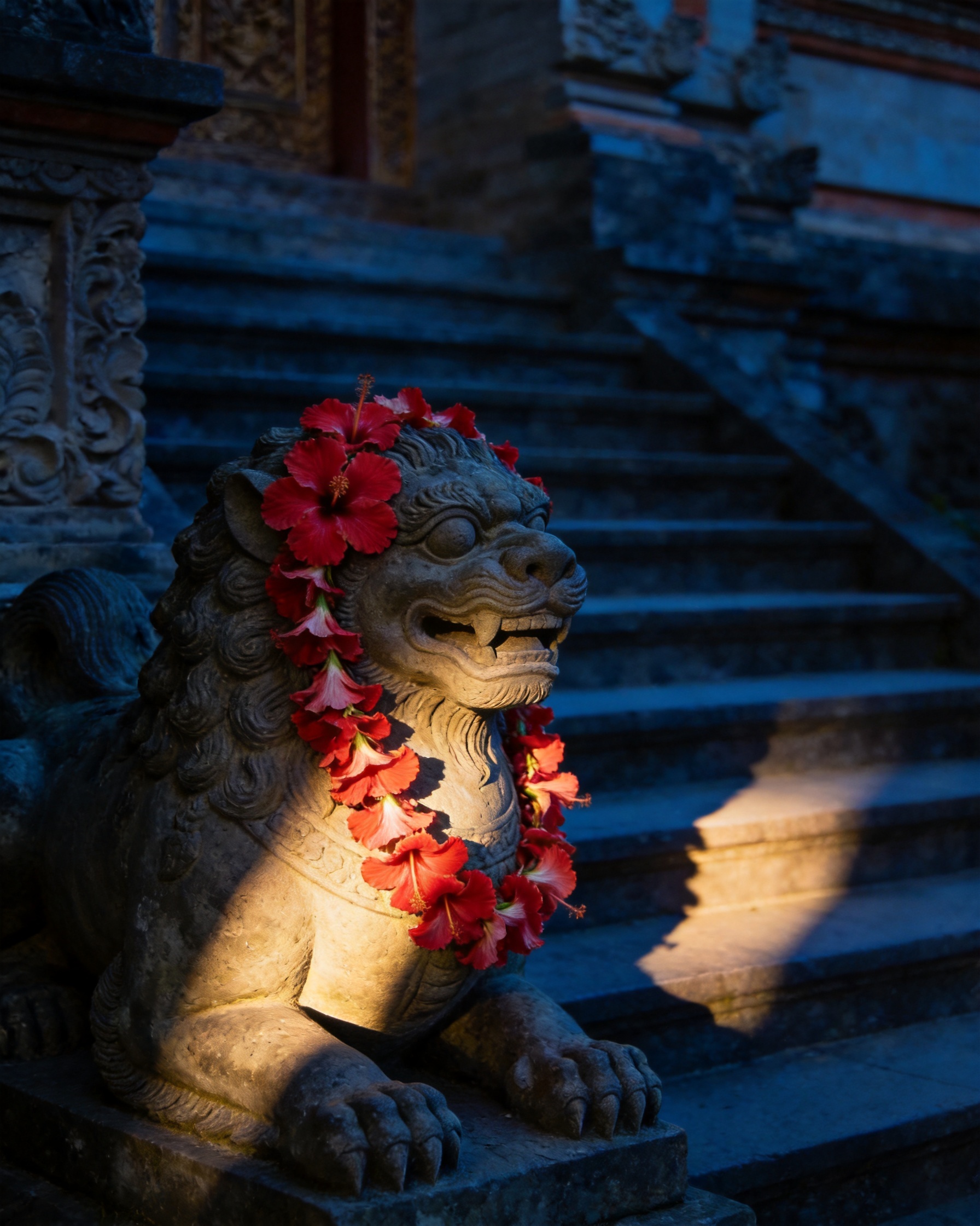 Carved stone lion guardian at temple steps with a red garland, lit by one hard shaft of late sun.