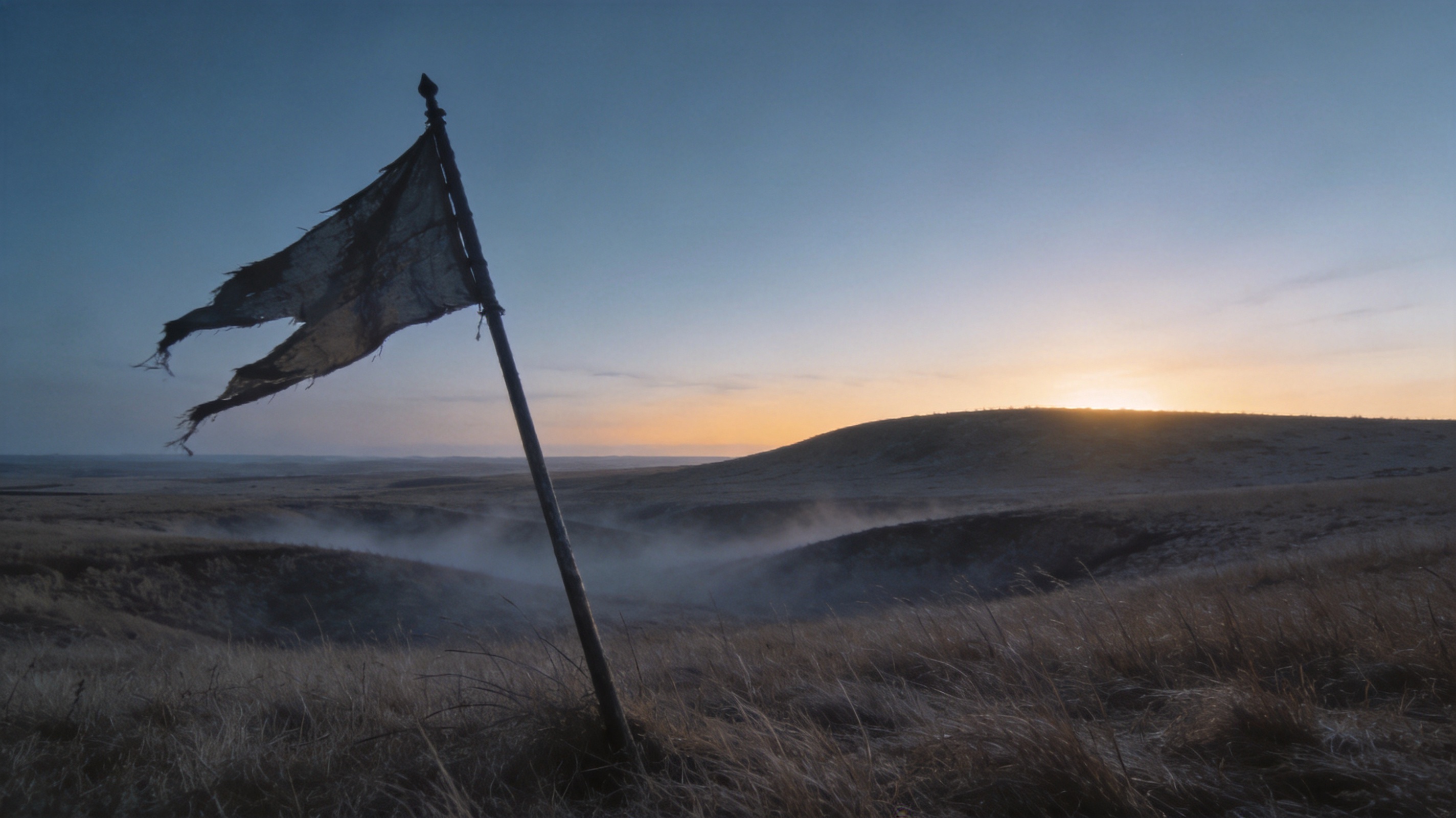 Empty windswept plain before sunrise with ground mist and a single tattered banner leaning in the foreground.