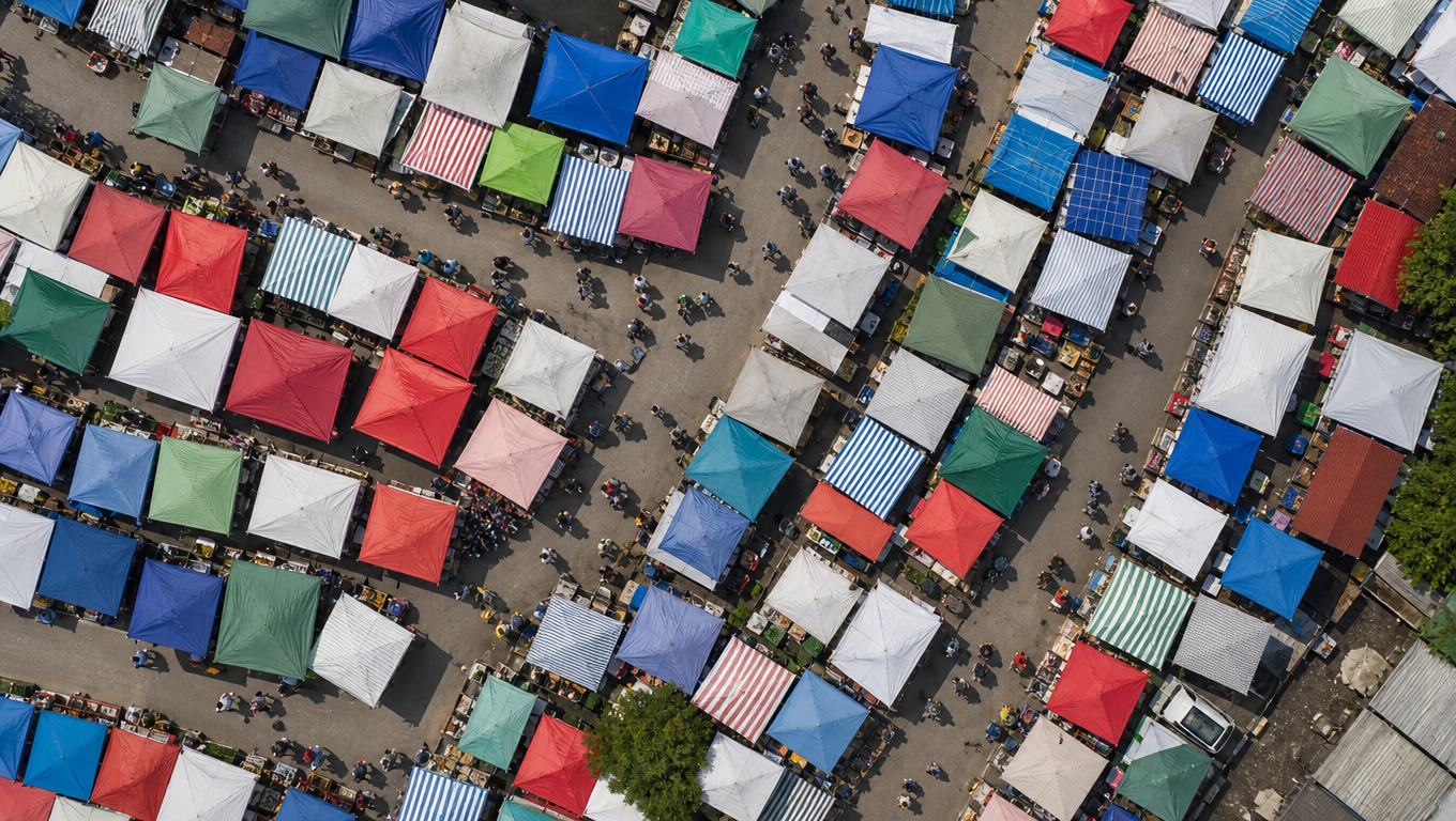 Aerial top-down view of a street market with rows of red, blue and striped awnings along a curving road.